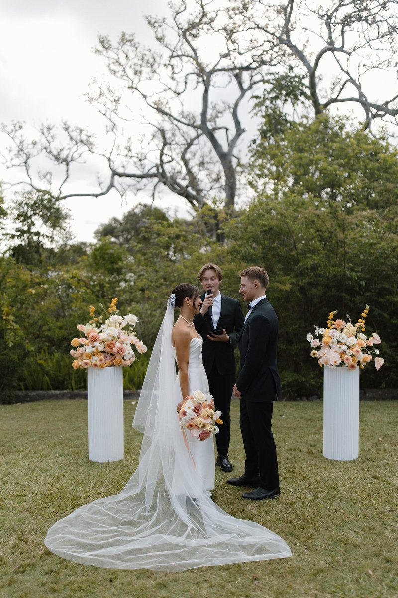 Couple at the altar with a long trailing veil, framed by flowers