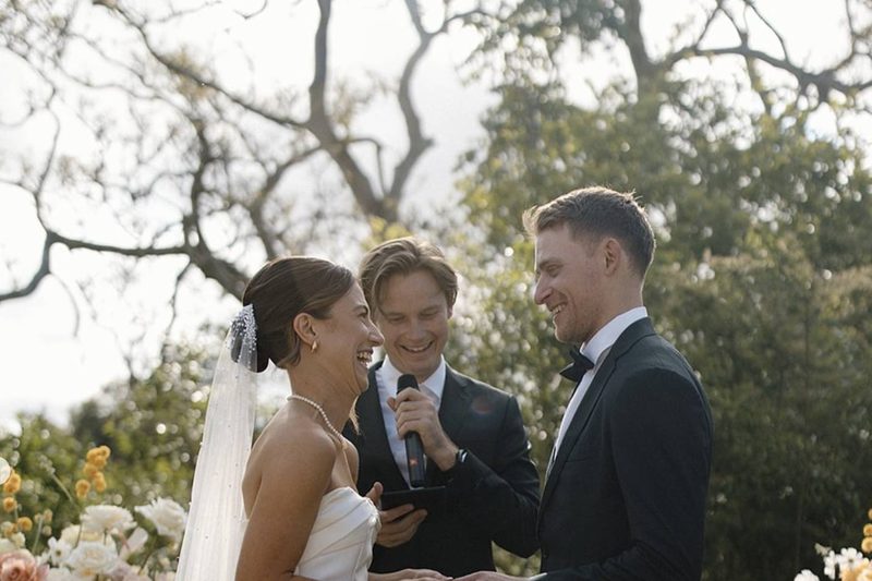 Brayden Wedd laughing with a couple mid-ceremony, microphone in hand