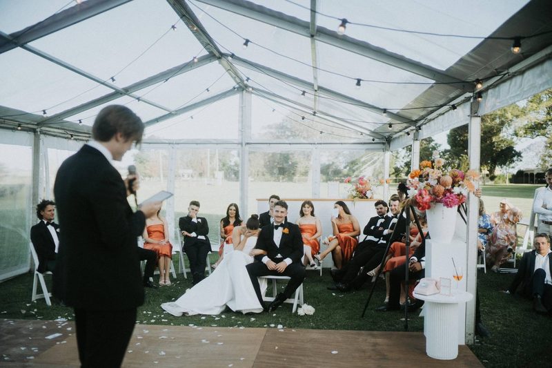 Brayden hosting speeches in a marquee as the couple looks on